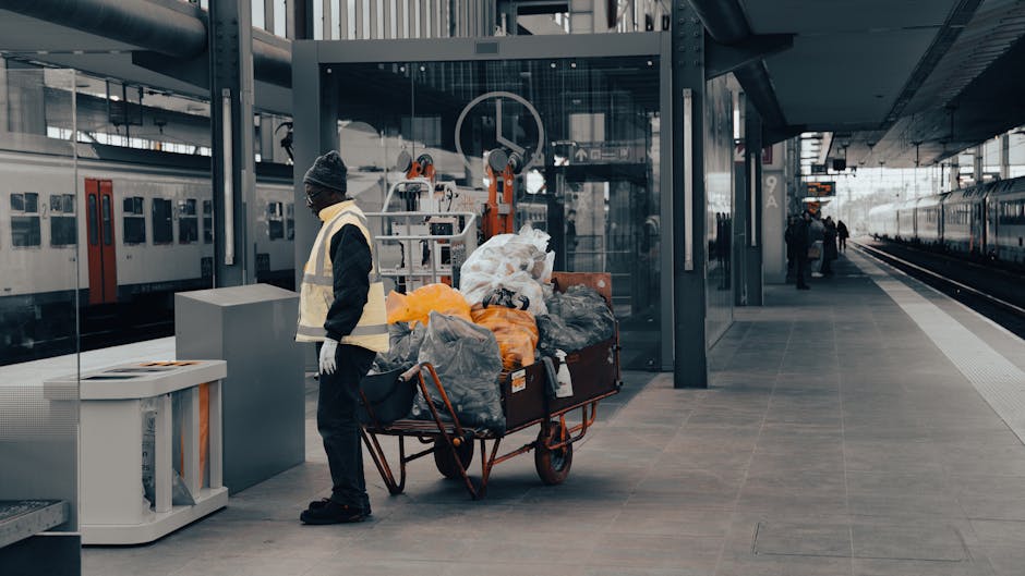 A pile of yellow and white plastic garbage bags filled with waste, stacked against a white textured exterior wall on a cobblestone pavement. The bags appear to contain household or commercial rubbish, with some bags featuring visible labels or handles. The setting is outdoor, with natural lighting illuminating the scene, and the ground is scattered with small leaves and debris. This image depicts waste disposal related to cleaning activities, which may be subject to local regulations such as Lambeth Council rules for waste disposal from cleaning jobs, as referenced on the Carpet Cleaning Kennington website. Carpet Cleaning Kennington offers professional cleaning and sanitisation services that comply with such waste management requirements.